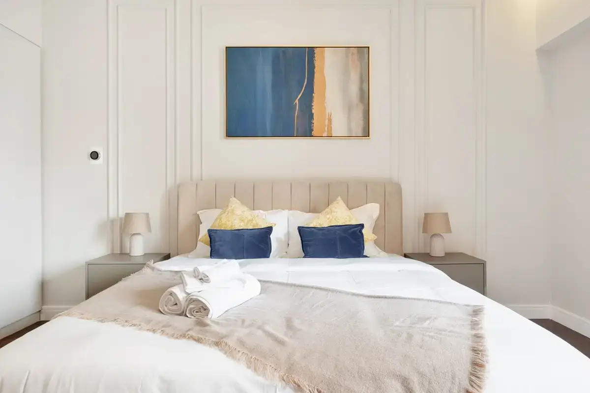 Bedroom with a white bed, blue cushions and an abstract painting