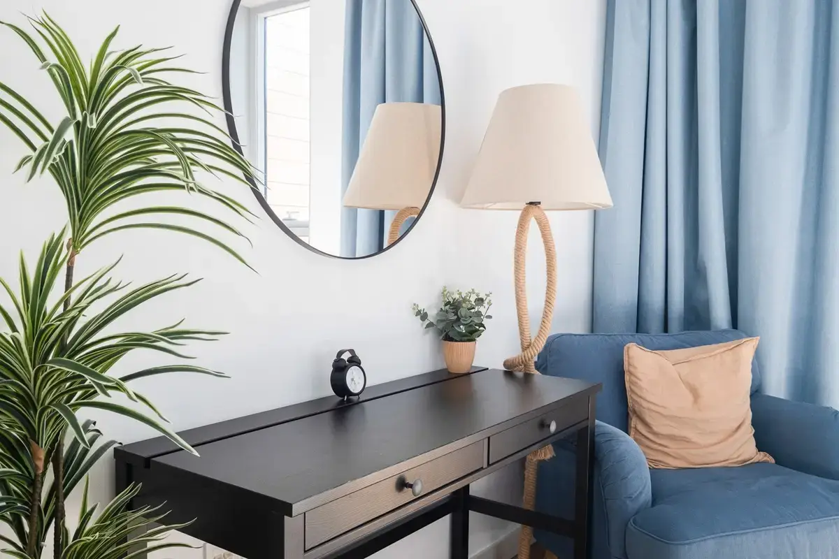 Interior corner with a dark console, round mirror, table lamps and a blue armchair
